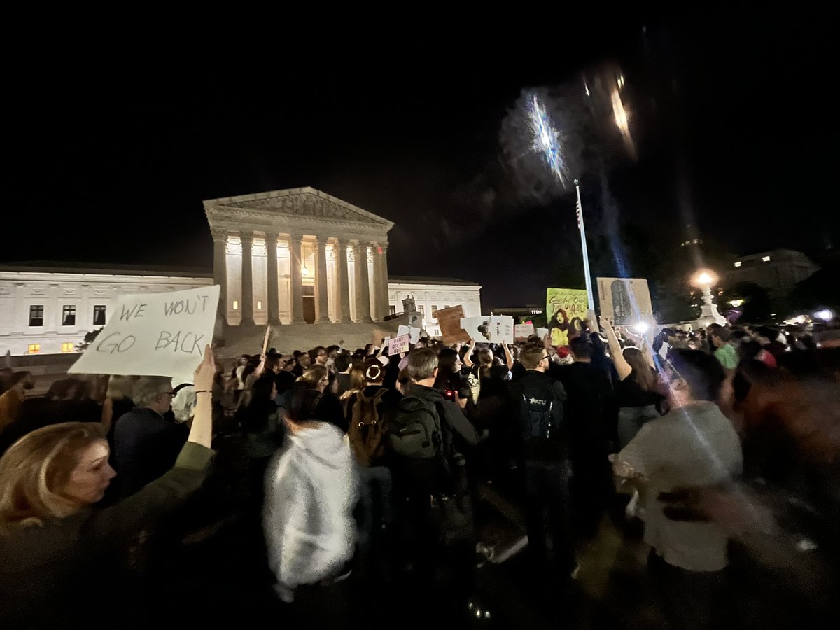 More scenes outside the U.S. Supreme Court.   Metal barricades surround the building. Approximately a dozen officers with the Supreme Court of the United States Police stand on the front steps, with more positioned along the perimeter.  DC Police stopping traffic