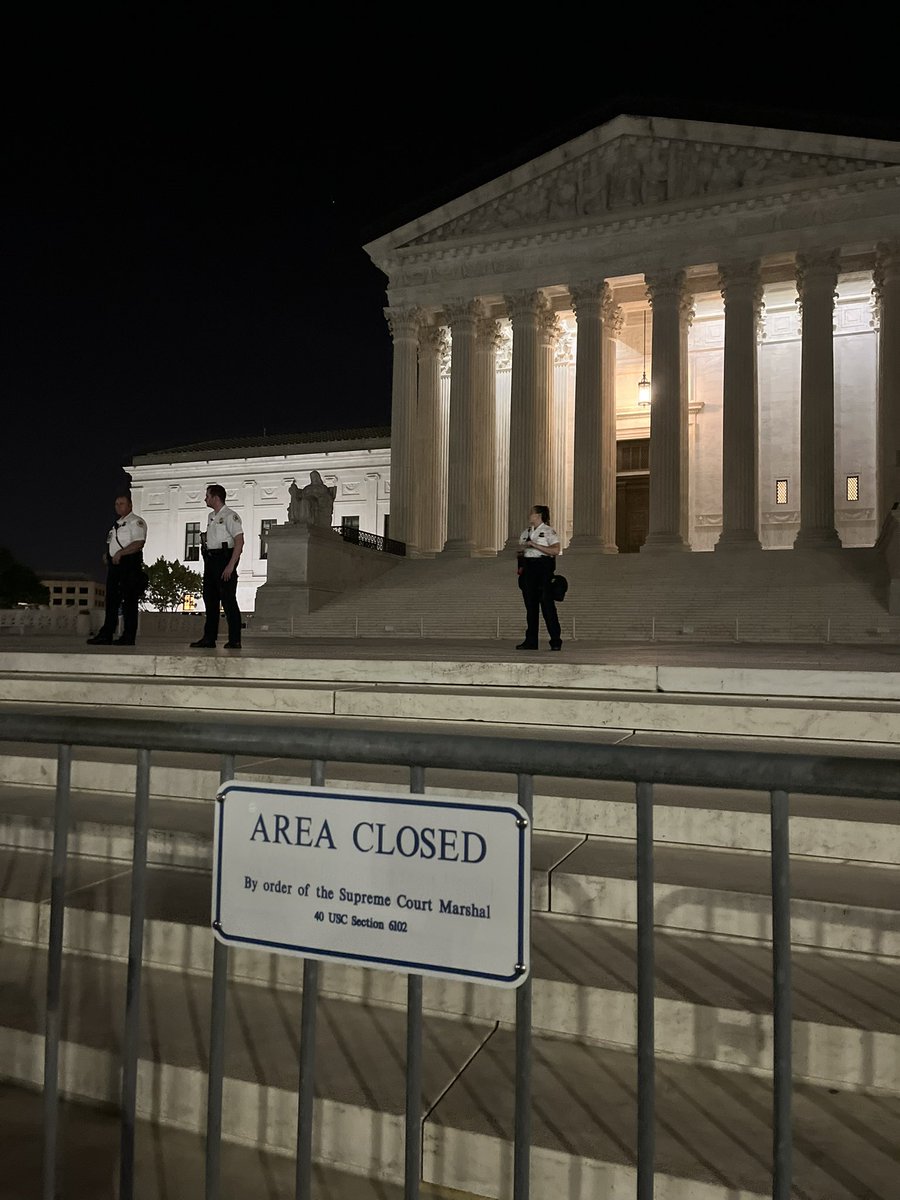 More scenes outside the U.S. Supreme Court.   Metal barricades surround the building. Approximately a dozen officers with the Supreme Court of the United States Police stand on the front steps, with more positioned along the perimeter.  DC Police stopping traffic