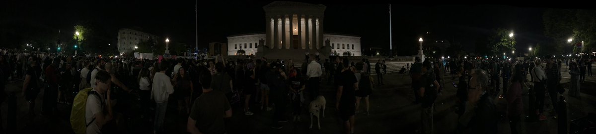 More scenes outside the U.S. Supreme Court.   Metal barricades surround the building. Approximately a dozen officers with the Supreme Court of the United States Police stand on the front steps, with more positioned along the perimeter.  DC Police stopping traffic